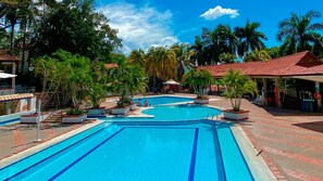 Una piscina con un borde de baldosas, rodeada de palmeras y estructuras cubiertas.