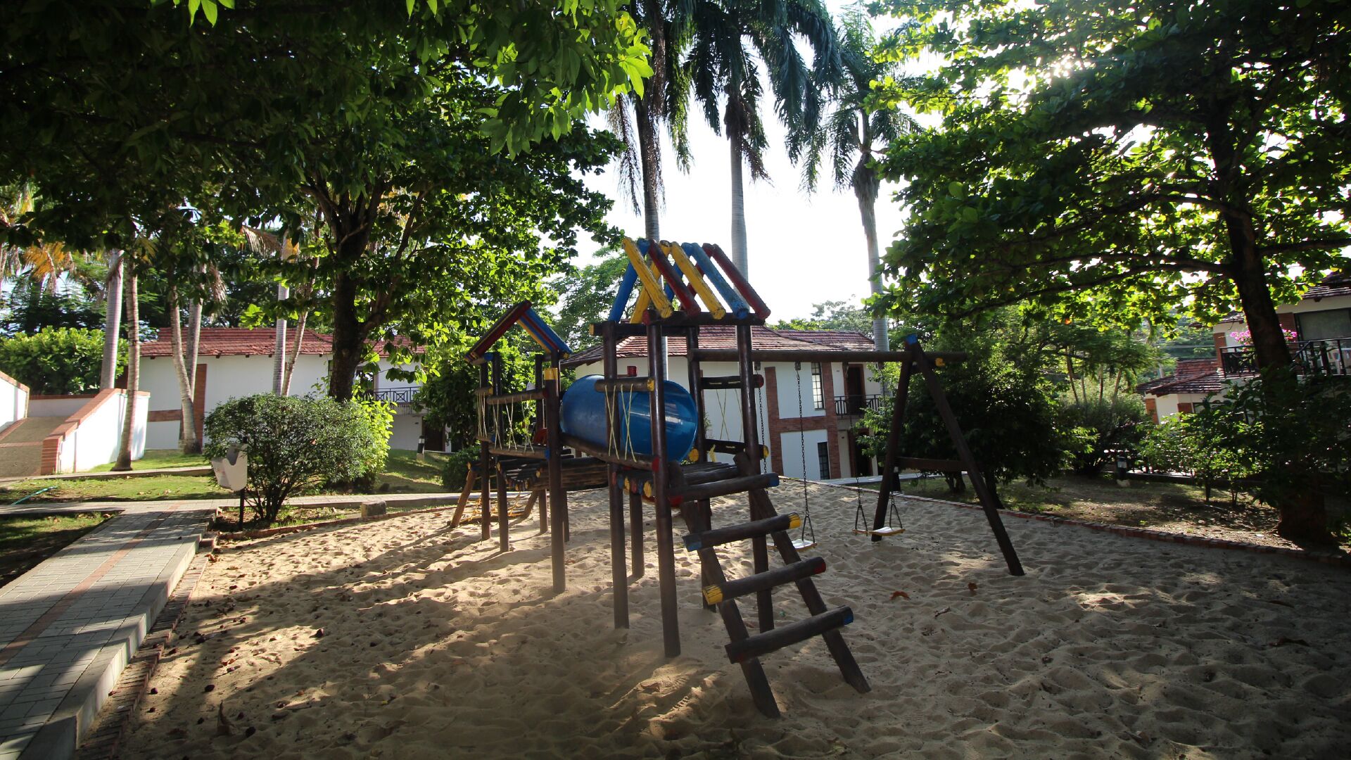 Un parque infantil con toboganes y estructuras para escalar, rodeado de arena y árboles.