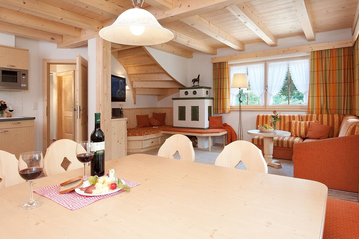 A cozy interior with a dining table set for two, a kitchen with modern appliances, and a living area with a sofa and a television.