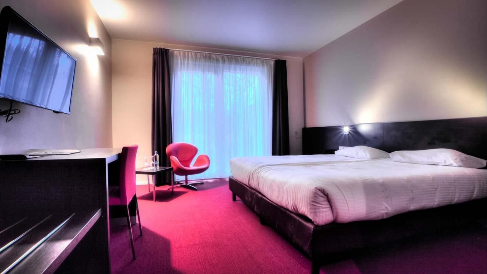 Une chambre d’hôtel équipée d’un lit, d’un bureau, d’une chaise et d’un téléviseur fixé au mur.