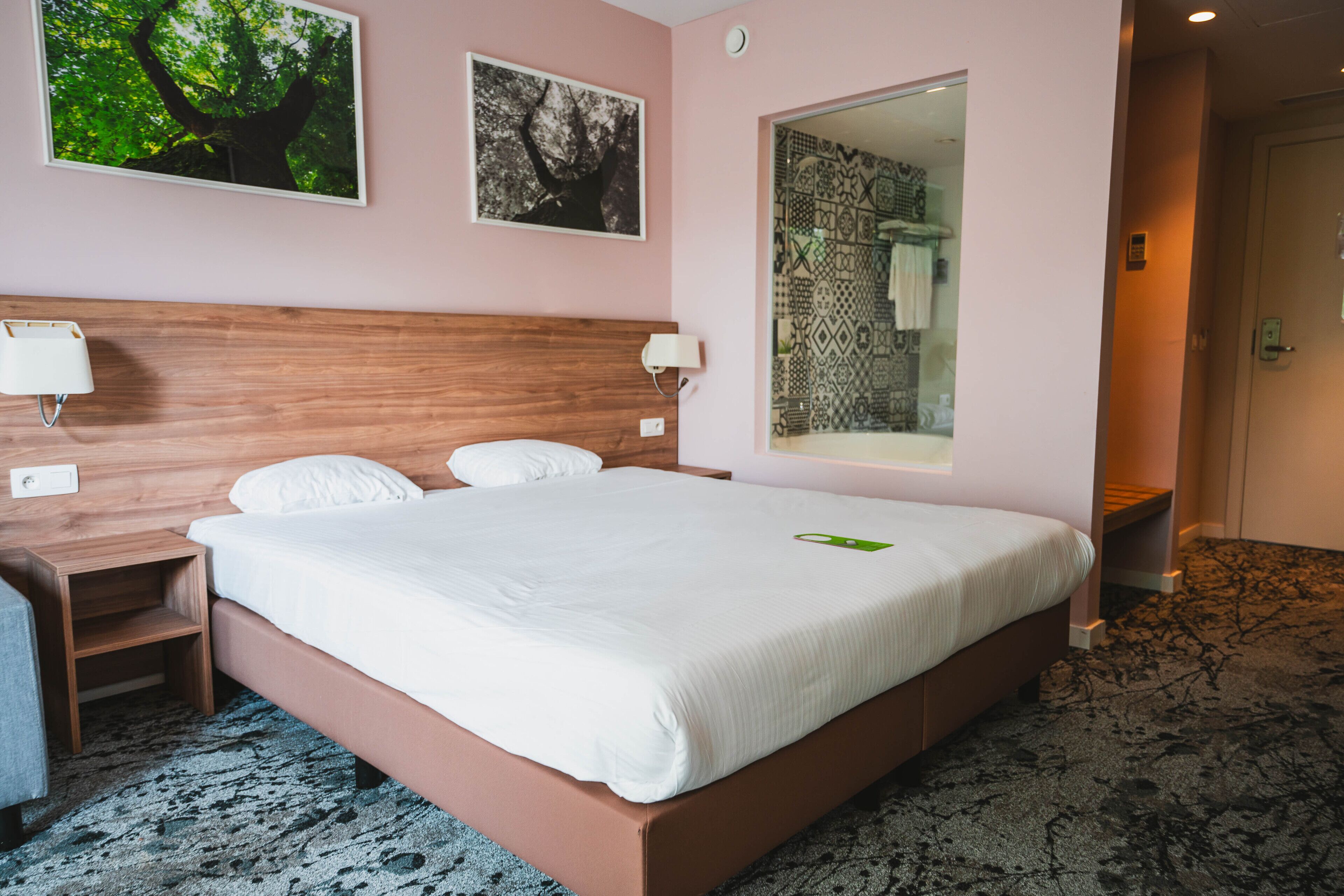 A hotel room with a large bed, a wooden headboard, two bedside tables with lamps, and a mirror on the wall.