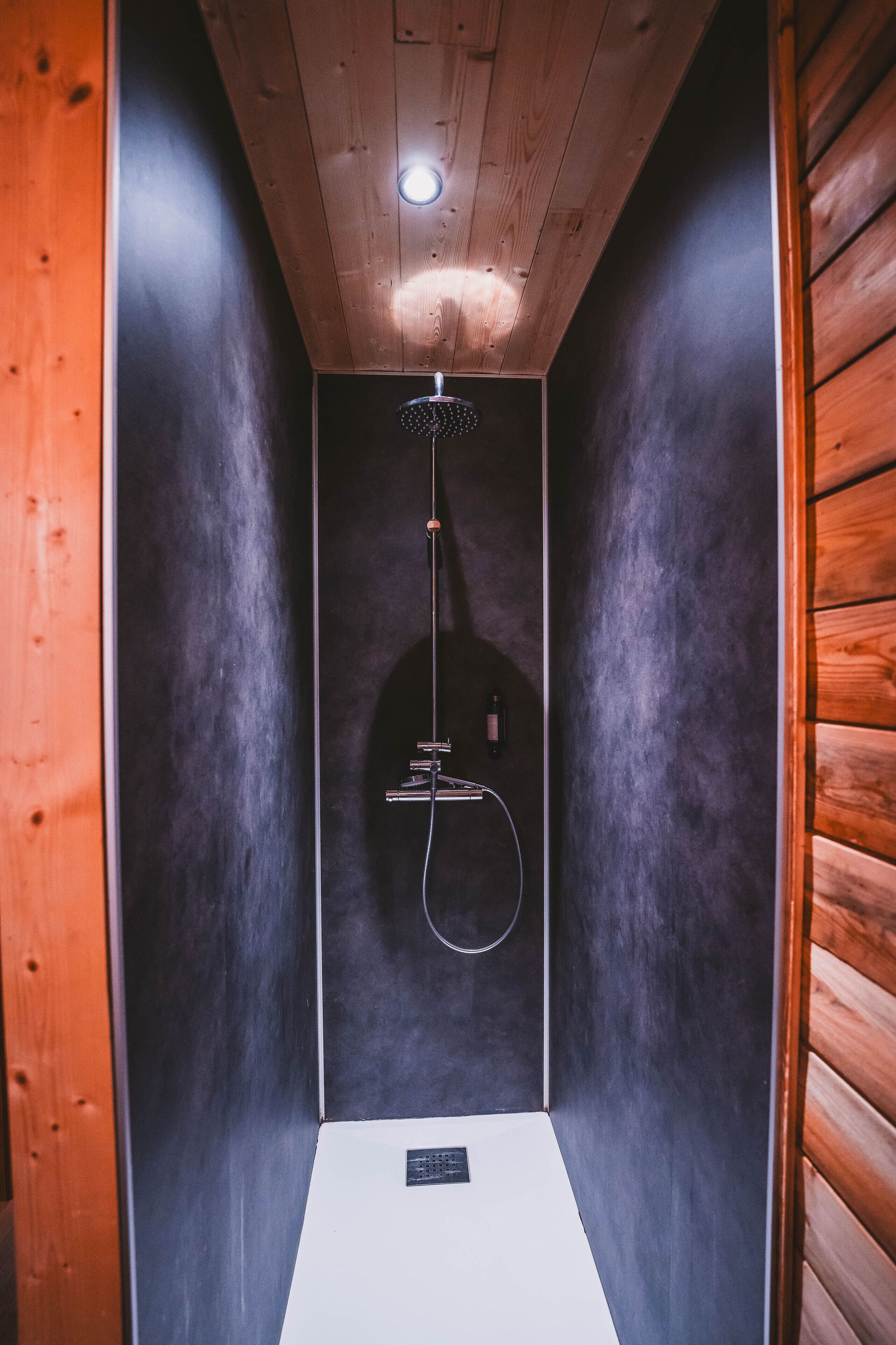 A small, enclosed shower area with a wooden ceiling and walls, a handheld showerhead, and a control panel.
