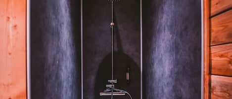 A small, enclosed shower area with a wooden ceiling and walls, a handheld showerhead, and a control panel.