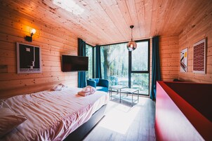 Une pièce de cabane en bois comprenant un lit, un téléviseur, une chaise bleue, une petite table et un banc rouge.