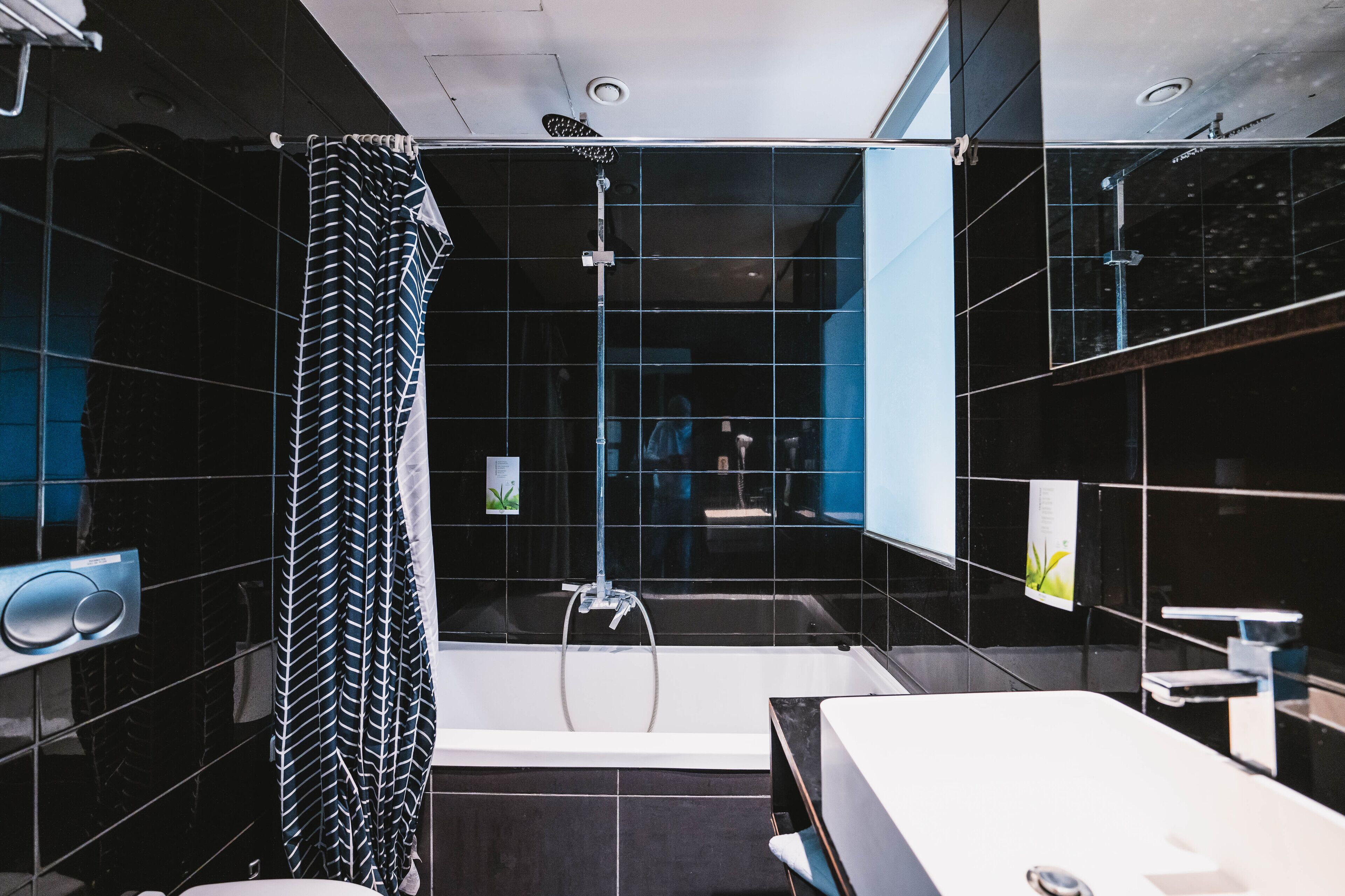 Une salle de bain moderne avec un rideau de douche rayé noir et blanc, une baignoire blanche et un grand miroir.