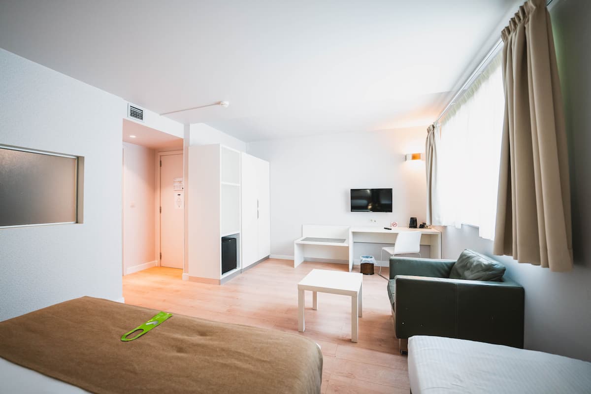 Une chambre d’hôtel moderne équipée d’un lit, d’un canapé, d’une télévision, d’un bureau et d’une kitchenette.