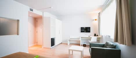 A modern hotel room with a bed, a sofa, a TV, a desk, and a kitchenette.