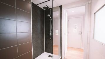 A modern bathroom with a glass-enclosed shower, dark tiled walls, and a visible door leading to another room.