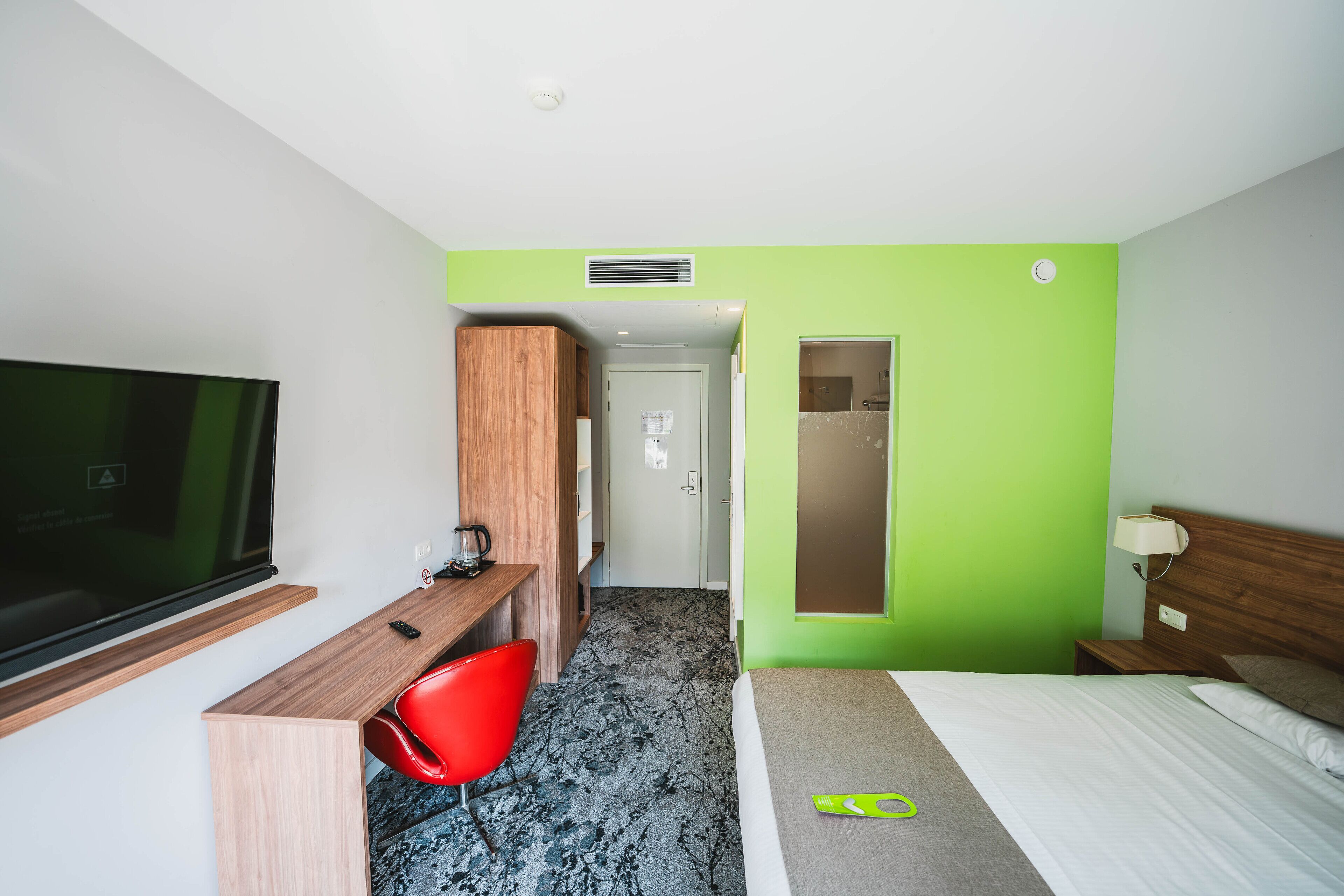 A hotel room with a bed, a desk with a chair, a television, and a door leading to another room.