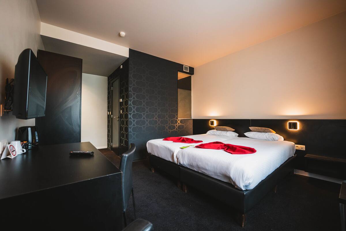 Une chambre d’hôtel moderne, dotée d’un grand lit, de tables de chevet, d’un bureau et d’une télévision.