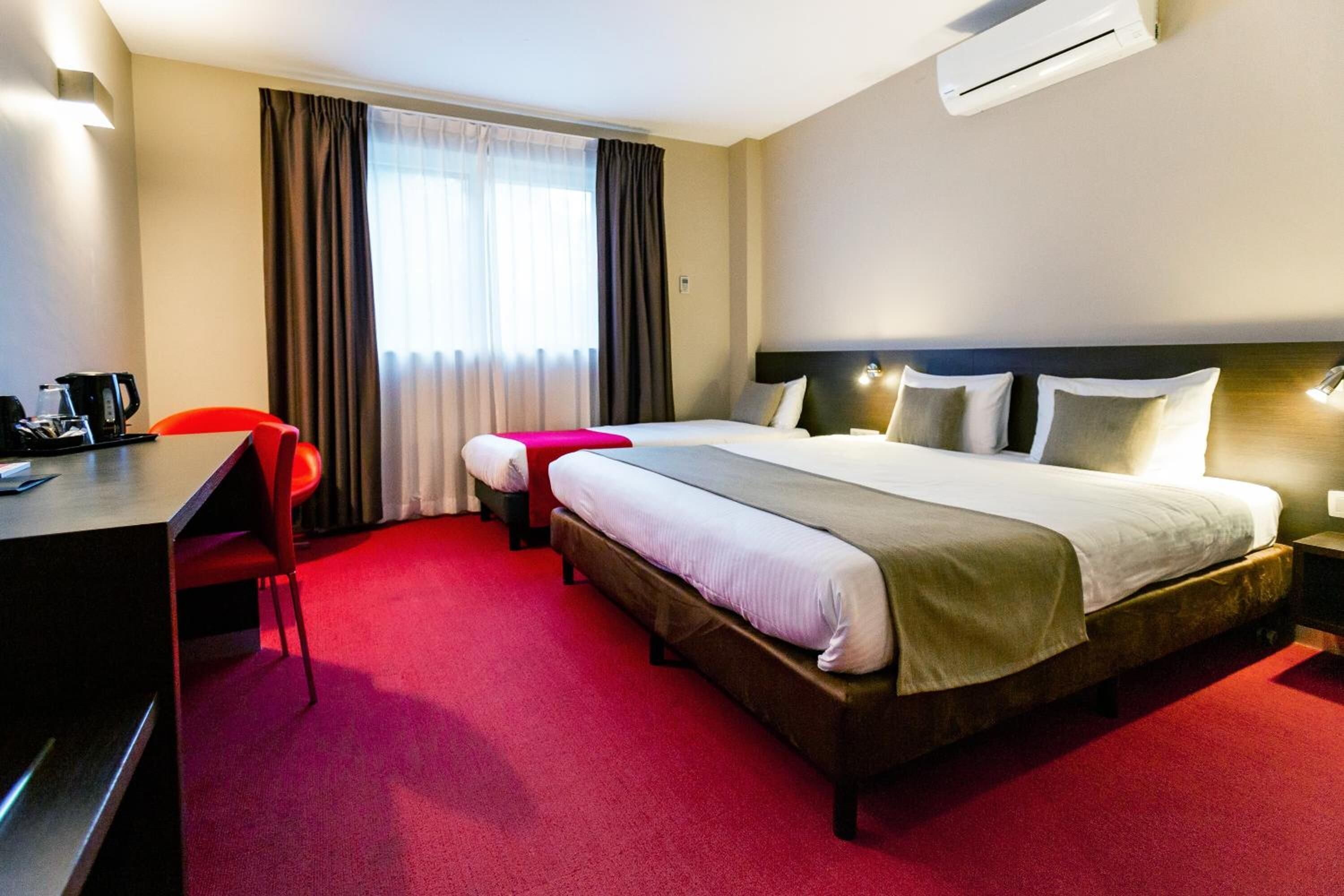 A hotel room with a large bed, a desk, a chair, and a window with curtains.