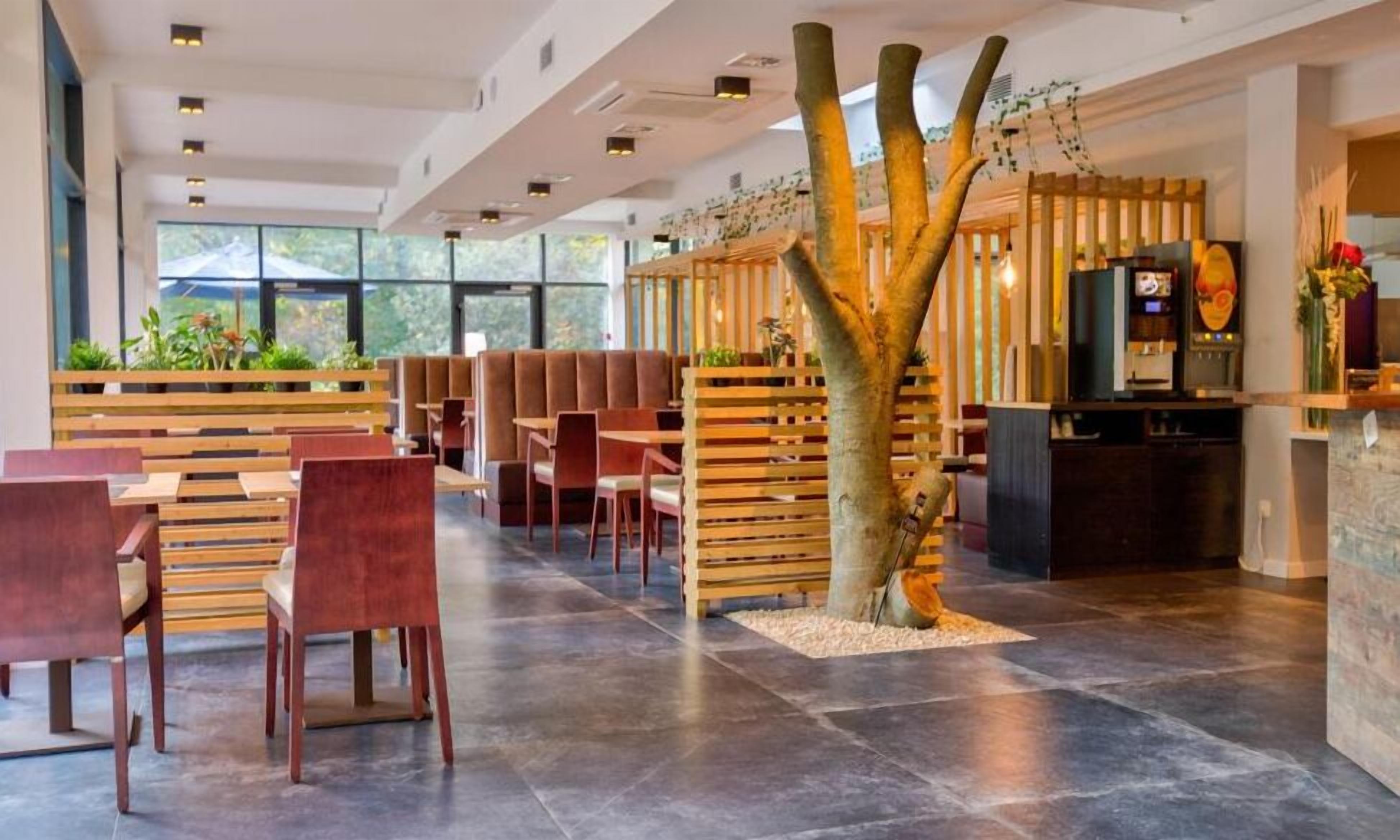 Een modern restaurant met houten meubilair, een boom als middelpunt en een bar.