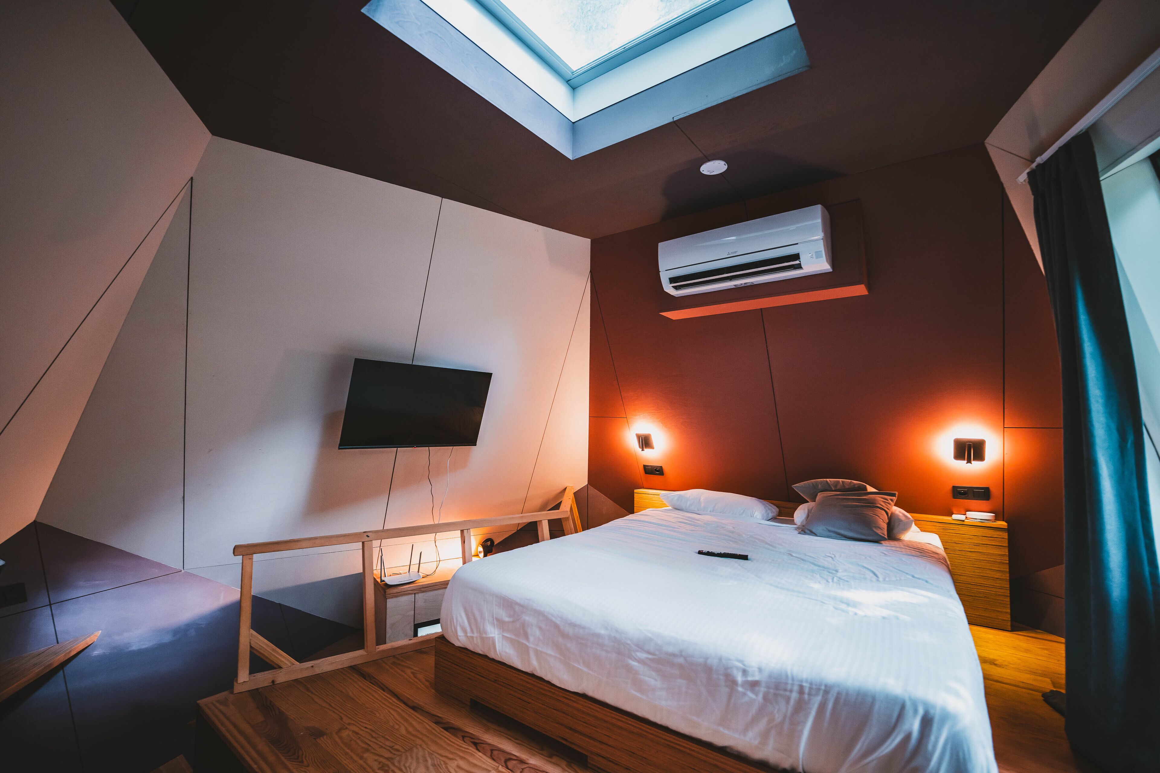 Een moderne slaapkamer met dakraam, een flatscreen televisie, nachtkastje en nachttafel.