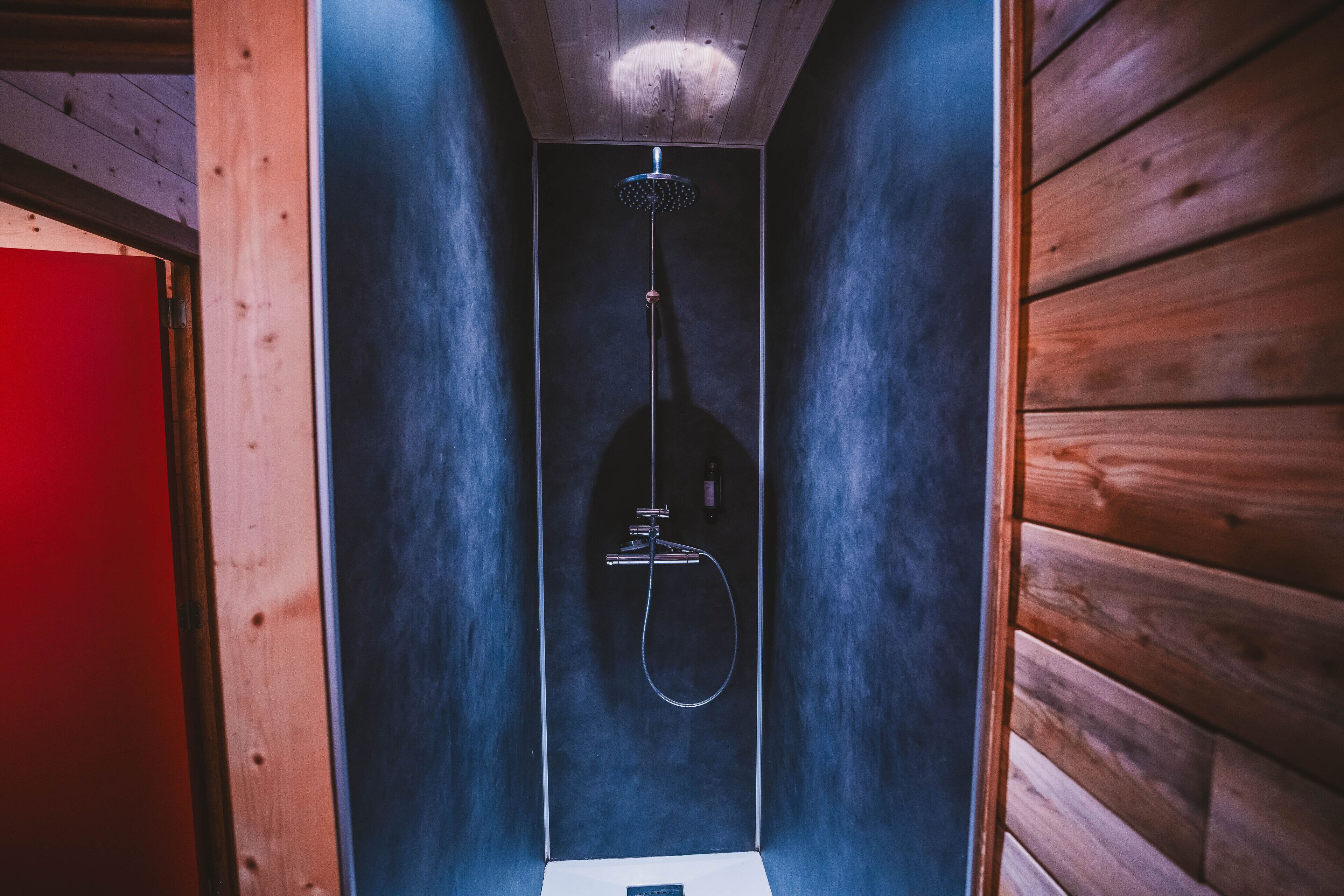 Un espacio de ducha estrecho y cerrado con techo y paredes de madera, un cabezal de ducha manual y un grifo de mano.
