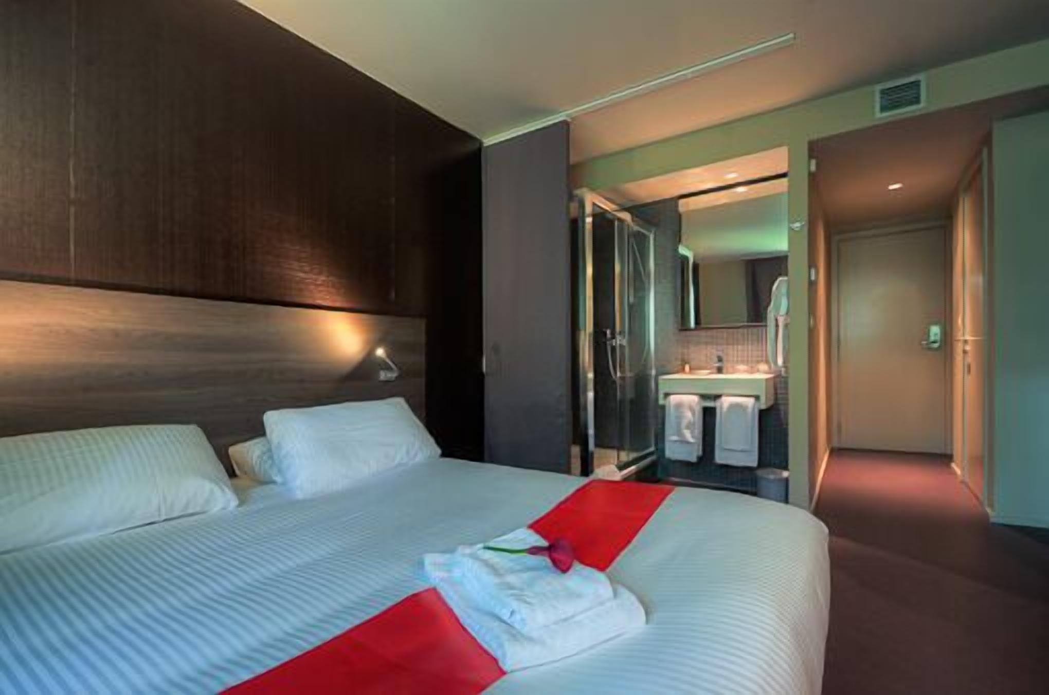 Una habitación de hotel moderna con una cama grande, un baño con ducha de vidrio y un pasillo que conduce a otra habitación.