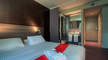 Una habitación de hotel moderna con una cama grande, un baño con ducha de vidrio y un pasillo que conduce a otra habitación.