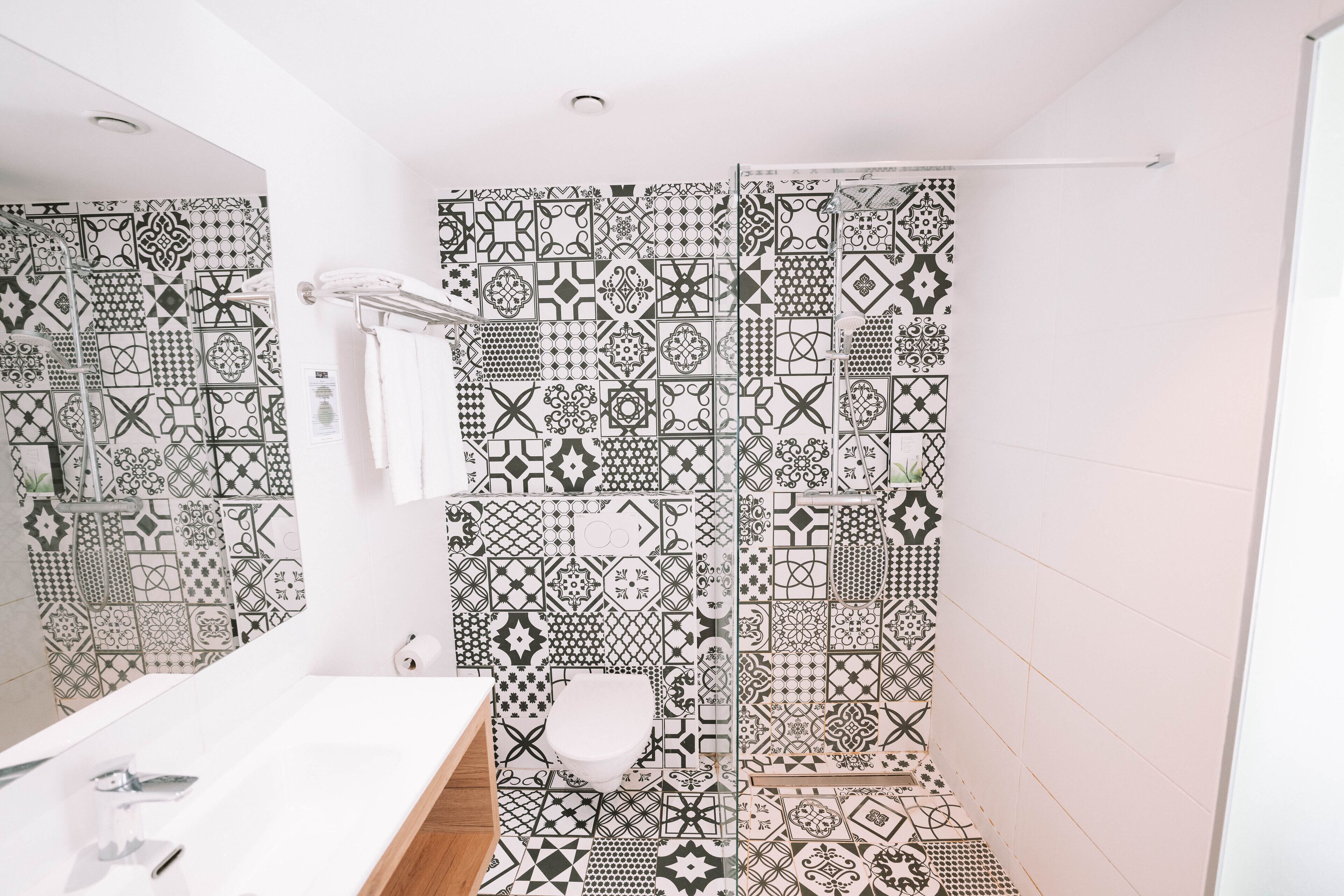 Une salle de bain avec un lavabo blanc, des toilettes et un espace douche agrémenté de carreaux à motifs.