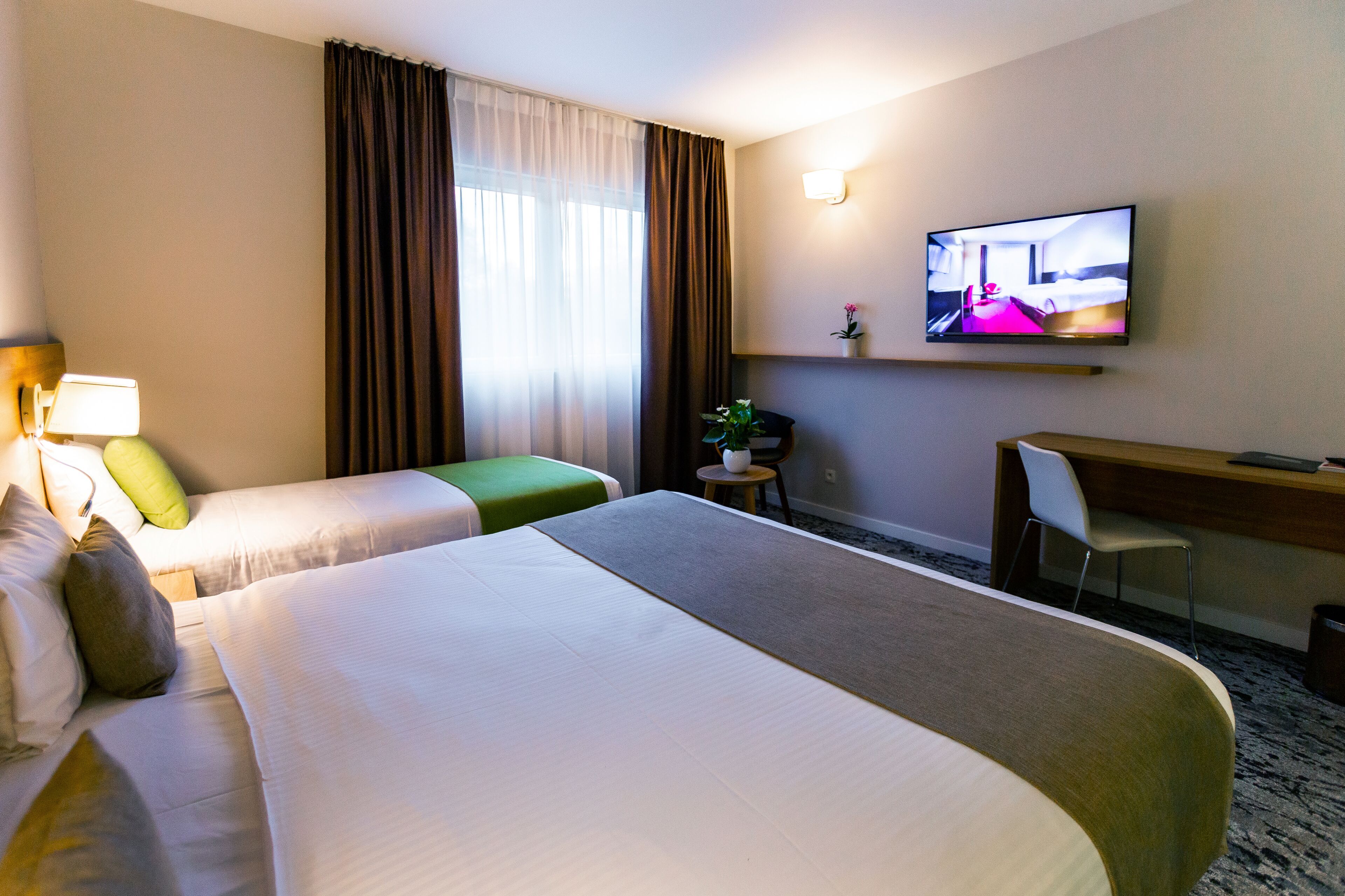 A hotel room with two beds, a desk, a chair, a television, and a small table with a plant.