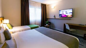 A hotel room with two beds, a desk, a chair, a television, and a small table with a plant.