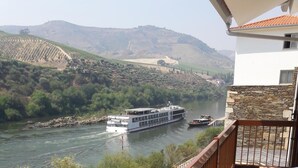 Un balcón con vista a un río, una embarcación y colinas circundantes.