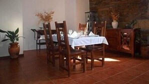 Un comedor con pared de piedra, sillas de madera, mantel blanco y plantas en macetas.