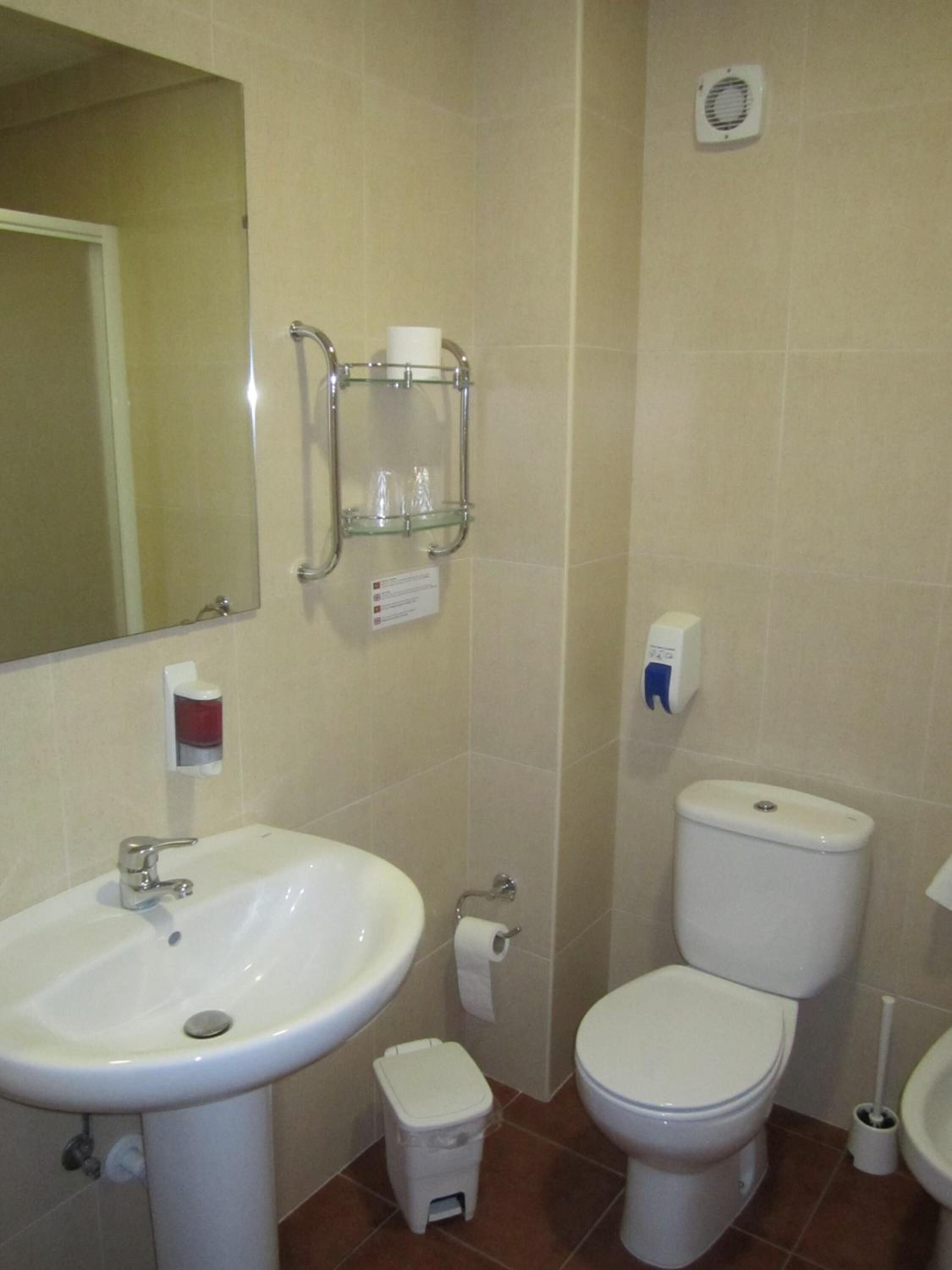 A bathroom with a sink, toilet, and a small trash bin.