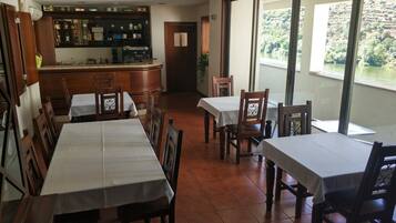Um restaurante com mesas e cadeiras de madeira, um espaço de bar com garrafas e copos, e vista para um rio.