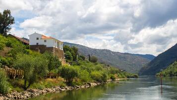 A white building with a red roof near a river, surrounded by greenery and hills.