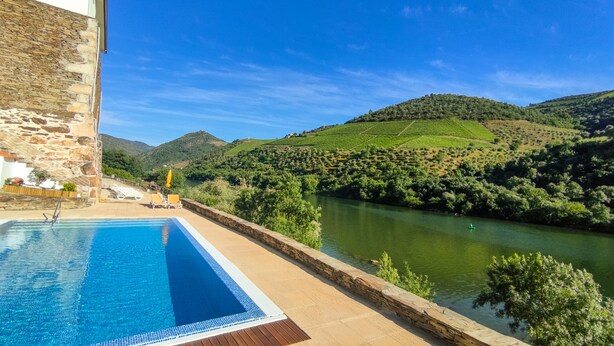 Una piscina con un muro de piedra y vistas a un río y colinas.