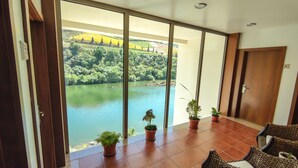 Un balcón con vistas a un lago y un bosque, plantas en macetas y mobiliario de mimbre.