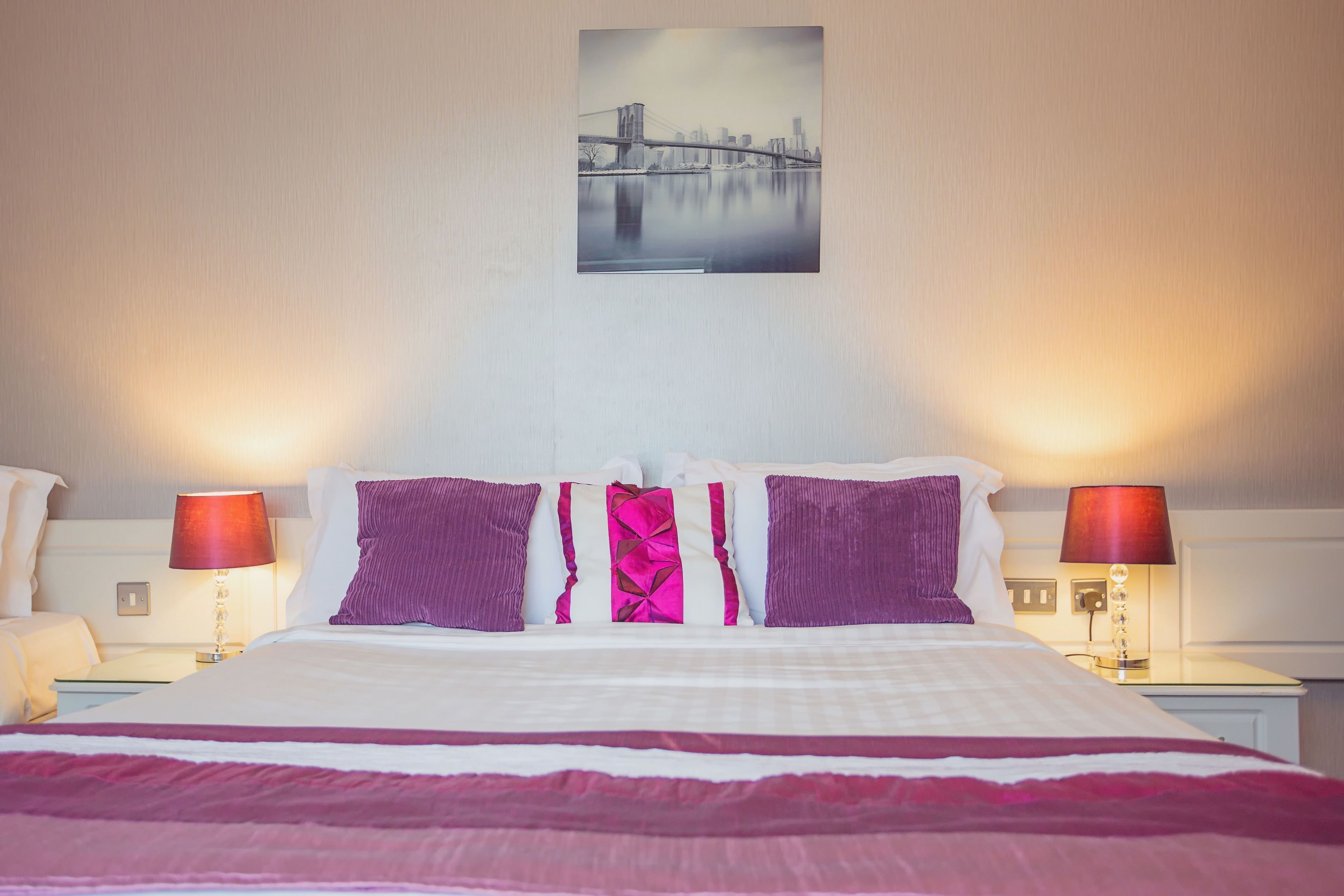 Habitación de hotel con cama, dos lámparas de noche y un cuadro de paisaje urbano en la pared.