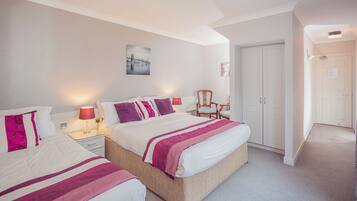 Une chambre d’hôtel avec deux lits, une table de chevet avec une lampe, une chaise et une armoire.