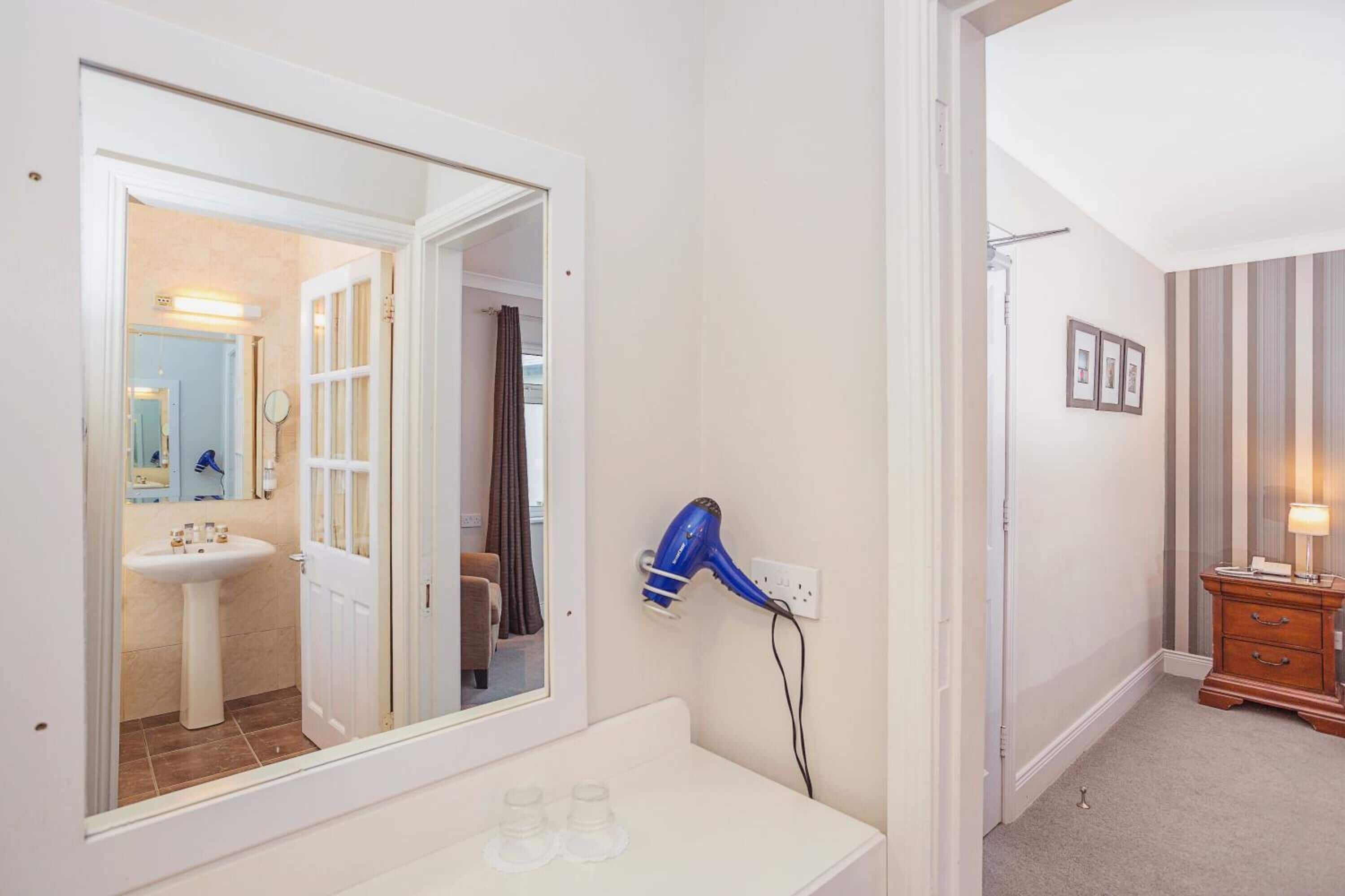 A bathroom with a white sink, mirror, and a blue hairdryer on a white countertop.