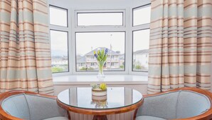 Ein Zimmer mit Erkerfenster, zwei Stühlen, einem kleinen runden Tisch und einem Topfpflanzen.