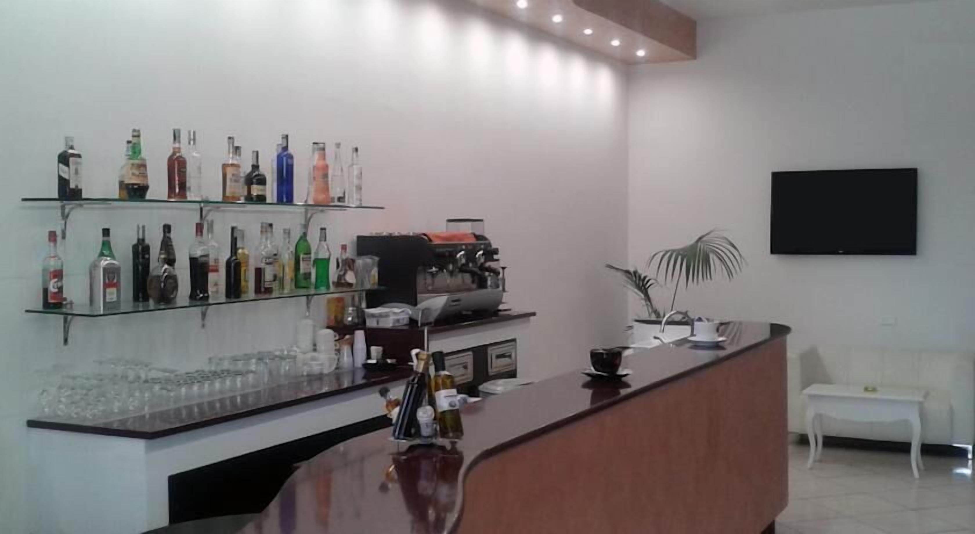 A bar area with shelves of liquor bottles, a coffee machine, and a TV mounted on the wall.