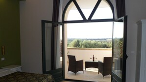 Una habitación de hotel con cama, un balcón con mesa y sillas, y vistas al campo.