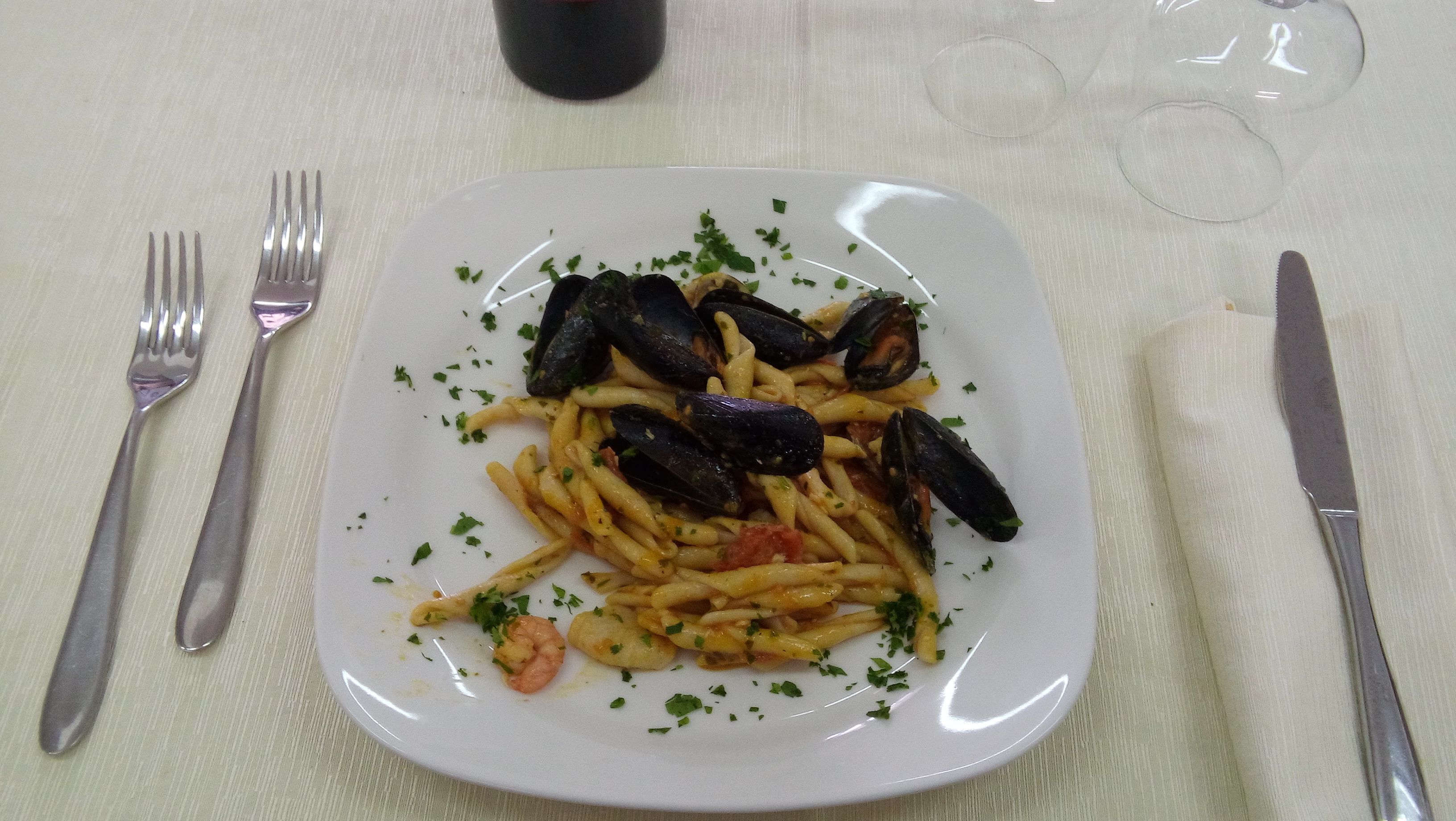 Un plato de pasta con mejillones y camarones, acompañado de un tenedor y un cuchillo sobre un mantel.
