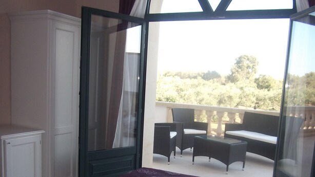 Een slaapkamer met een groot bed, een balkon met tuinmeubilair en uitzicht op de omgeving.