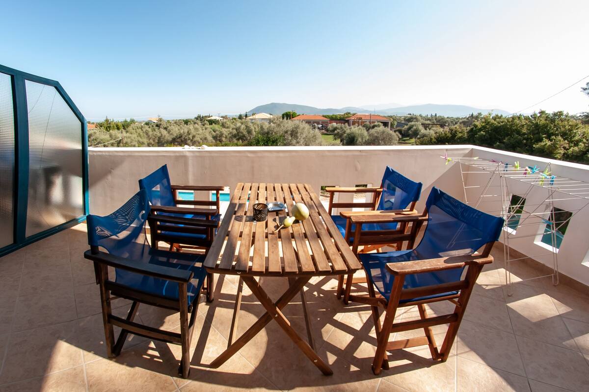 A rooftop terrace with a wooden table and chairs, a drying rack, and a view of the countryside.