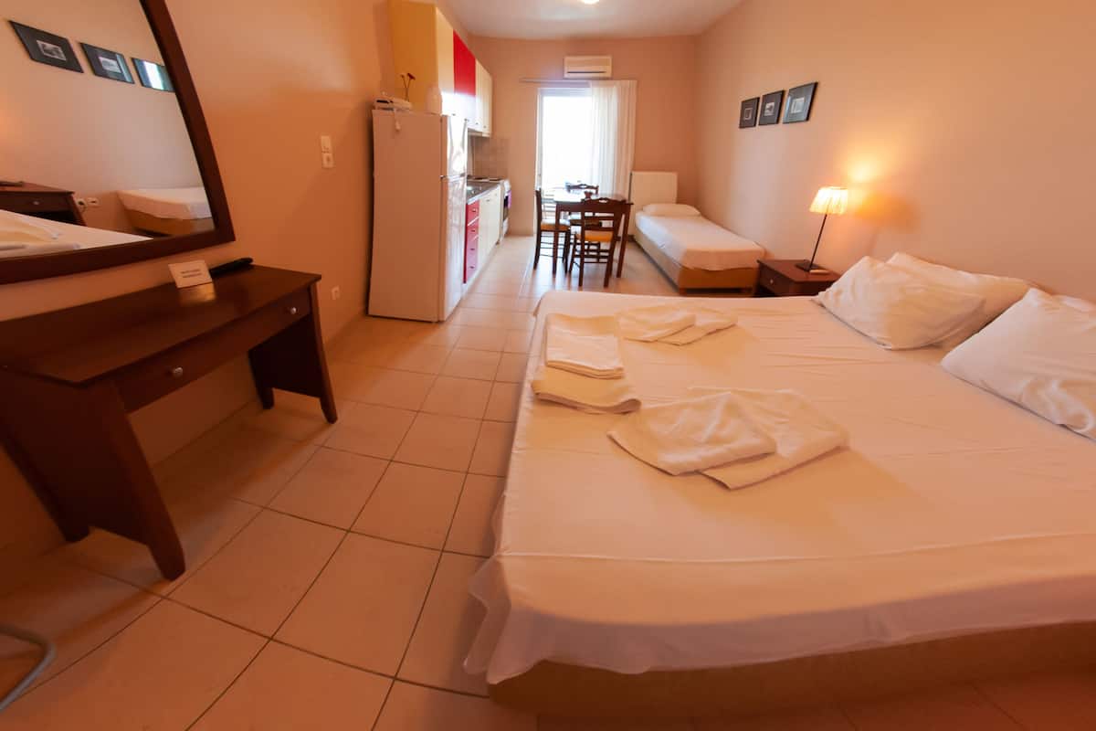 A hotel room with a bed, a desk, a chair, a small kitchenette, and a bathroom.