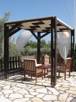 A covered outdoor seating area with wooden furniture and a stone-tiled floor. - Apartments Ithaki Holidays (Lefkada)