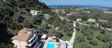 An aerial view of a property with a swimming pool, a covered patio, and a view of the sea.