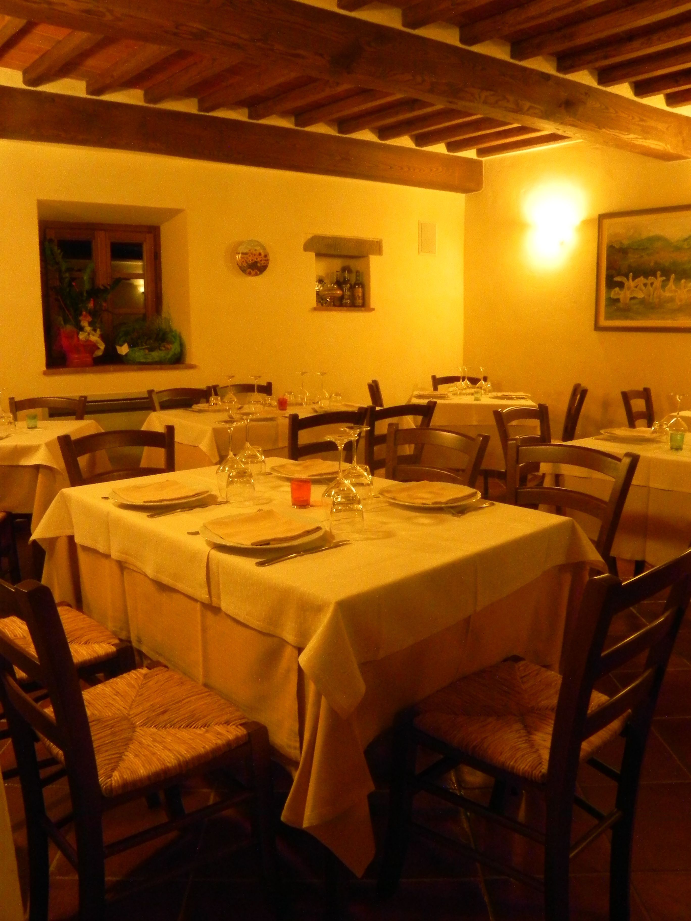 A dining area with round tables set for four, each with white tablecloths, chairs, and dinnerware.