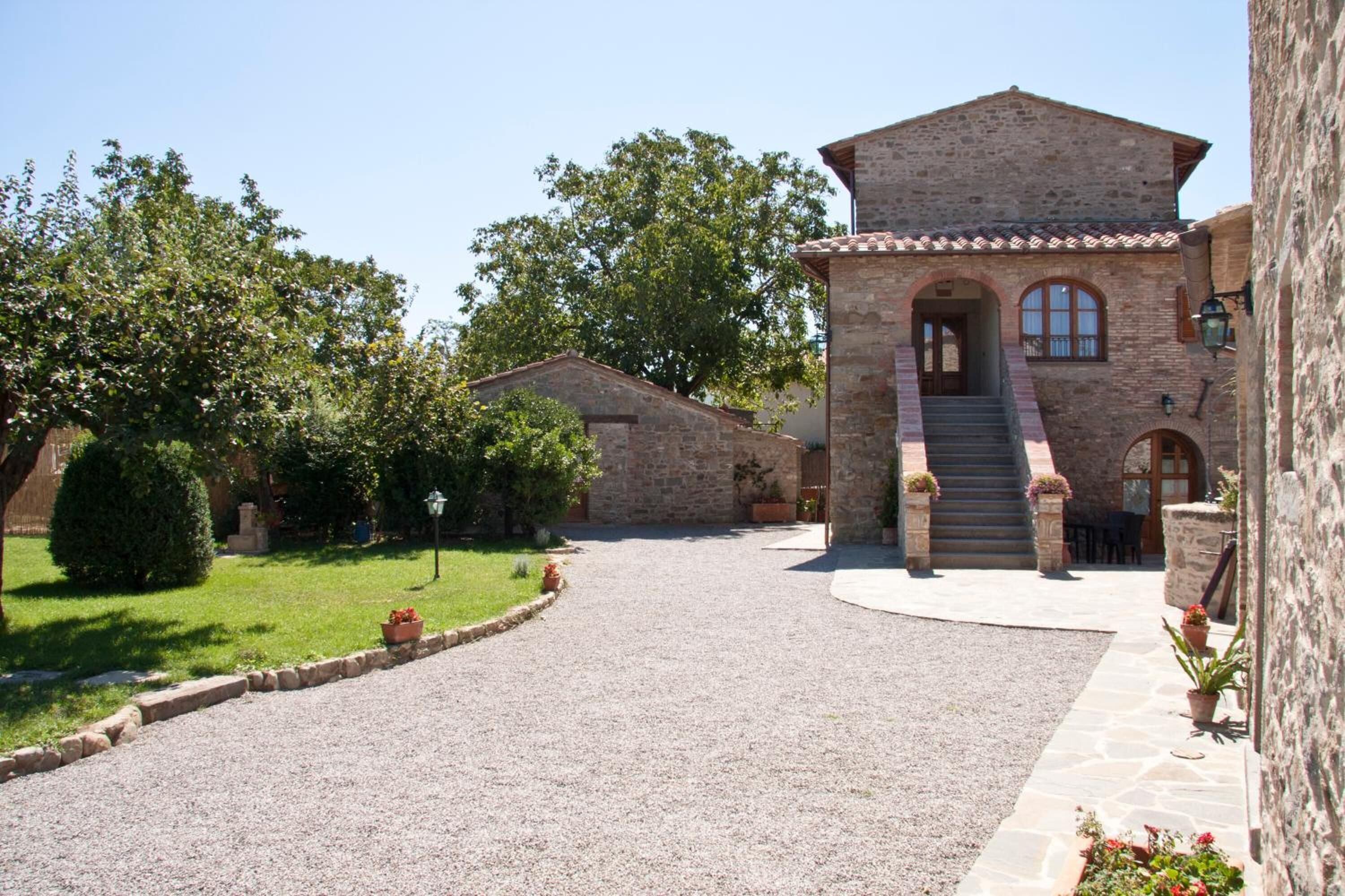 A stone building with a central staircase leading to an entrance, surrounded by a gravel driveway and greenery.