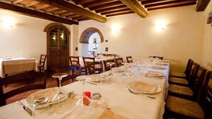 Ein Essbereich mit einem langen Tisch, gedeckt für eine Mahlzeit, Holzbalken an der Decke und rundbogigen Durchgängen.