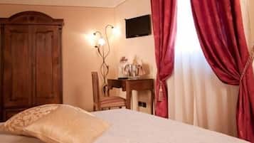 A hotel room with a bed, a wooden wardrobe, a desk with a chair, and a TV mounted on the wall.