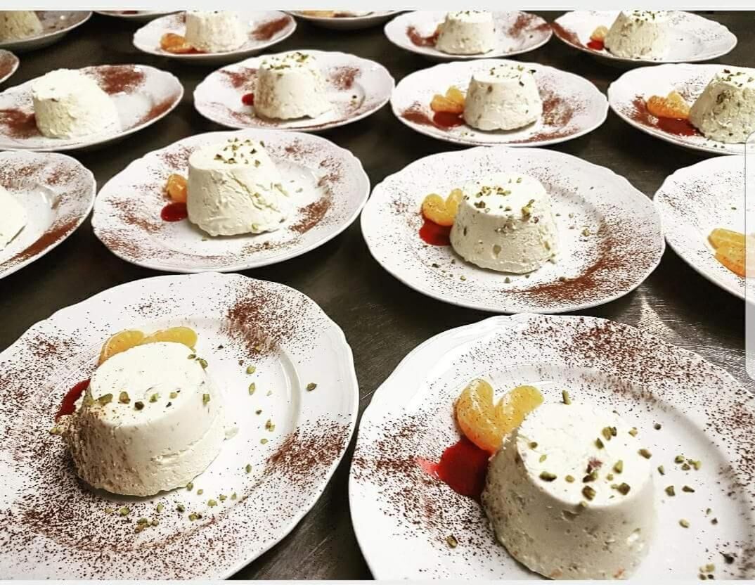 Multiple plates of dessert with white creamy substance, garnished with nuts and dusted with a red powder, arranged on a dark surface.