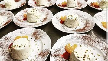 Multiple plates of dessert with white creamy substance, garnished with nuts and dusted with a red powder, arranged on a dark surface.