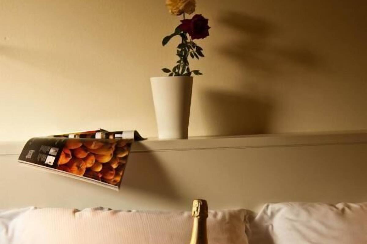 Una cama con una colcha estampada, una botella de champán y una copa de champán sobre una bandeja. Hay un florero con flores en un estante sobre la cama.