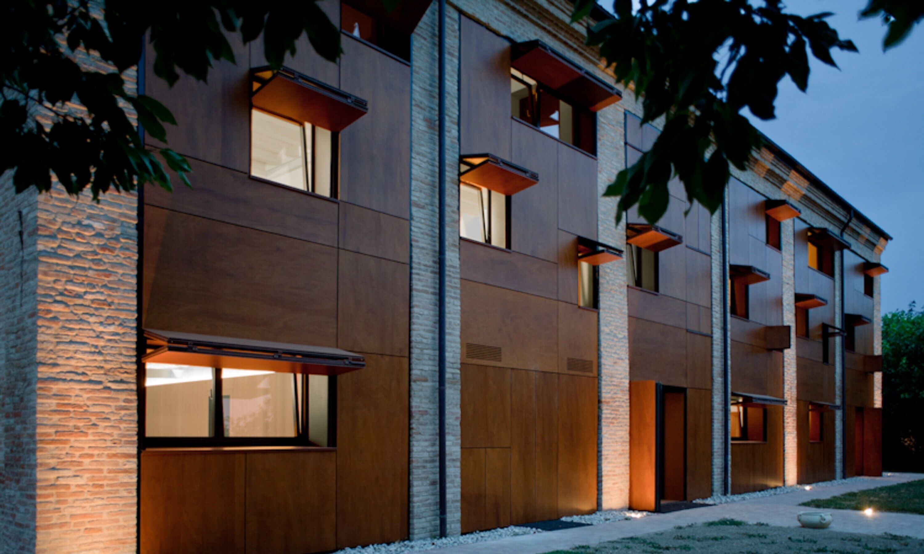 Un edificio moderno con numerose finestre e balconi, caratterizzato da un rivestimento misto in mattoni e legno.